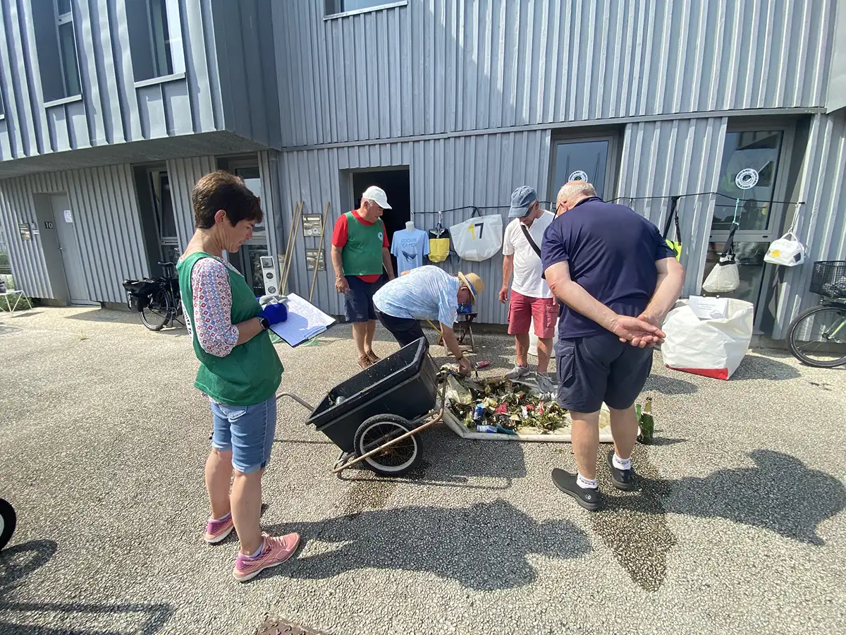 Groupe de bénévoles réunis autour d’une brouette pleine de déchets ramassés dans le port de La Rochelle, en train de trier et comptabiliser la collecte.