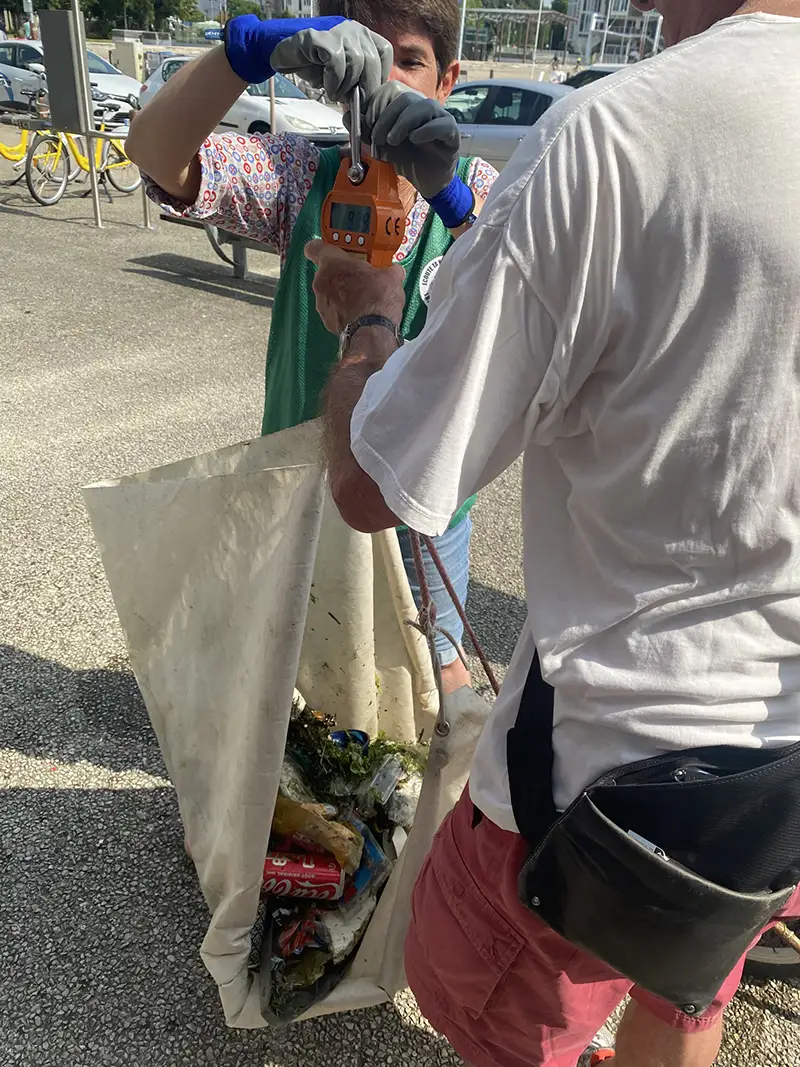 Deux bénévoles trient les déchets collectés, déposés dans un grand sac en toile, lors de l’opération de nettoyage du port de La Rochelle.
